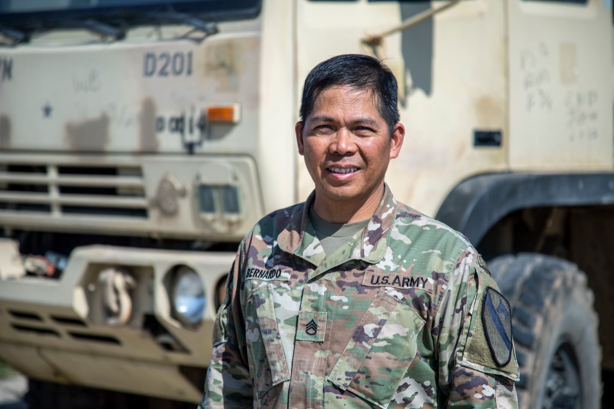 An Asian American Army sergeant first class standing beside a tactical truck