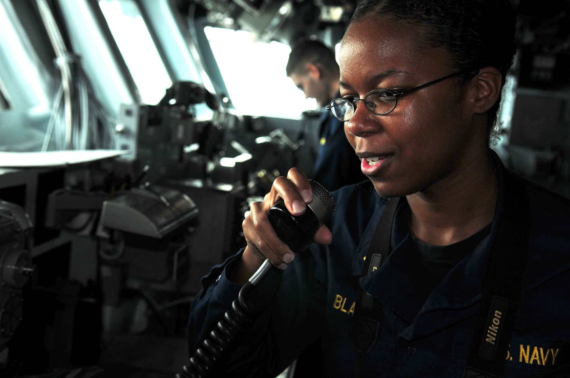A Black woman Navy officer speaking on the 1MC from a ship's bridge