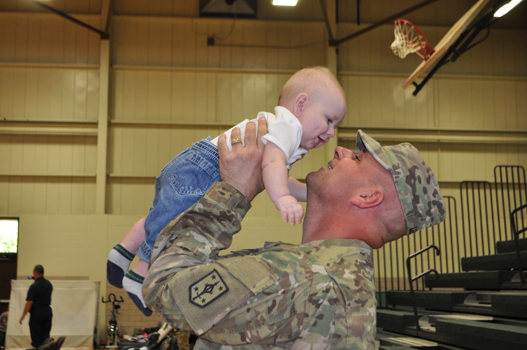 A soldier in uniform lifts his baby daughter after a homecoming
