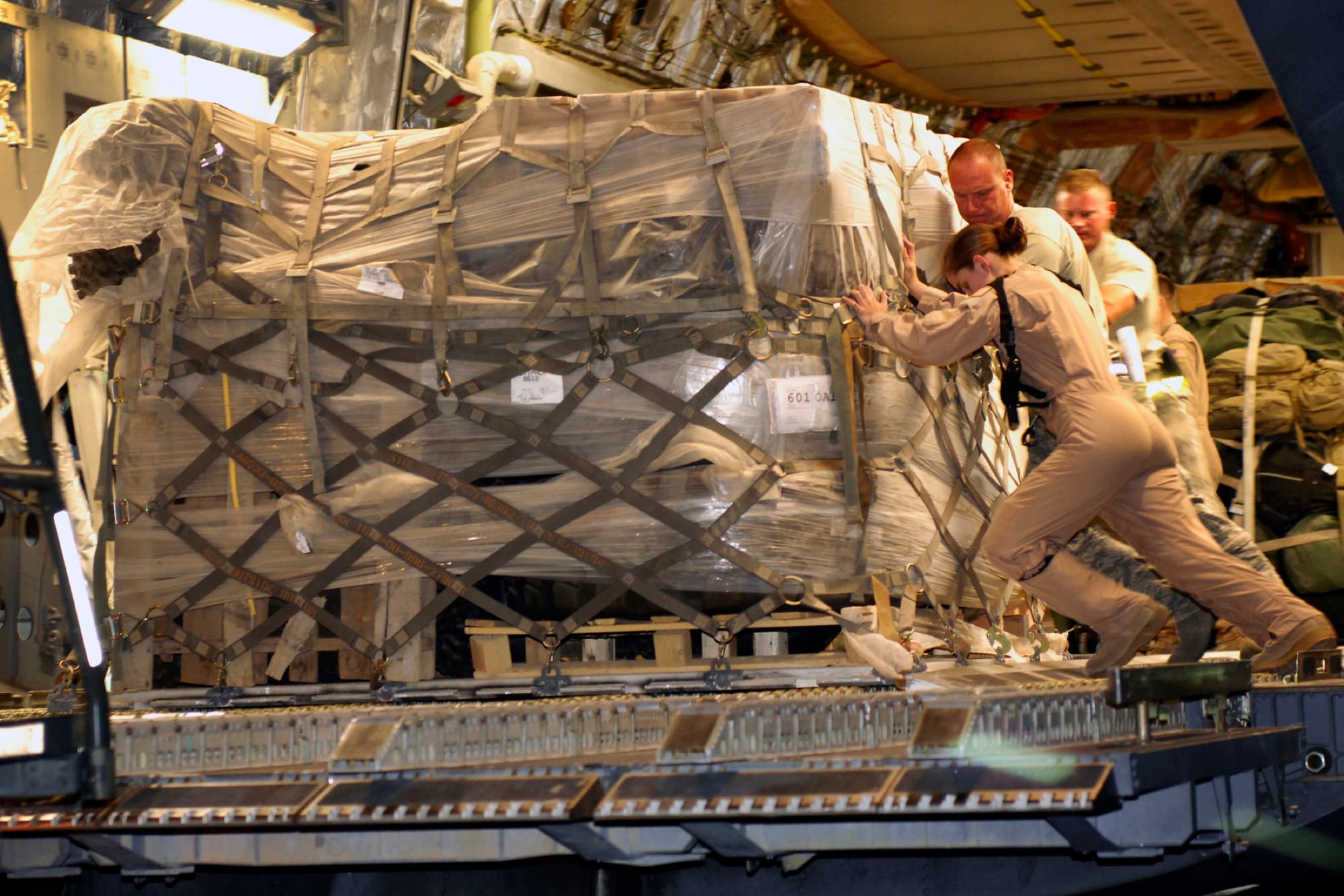 Airmen, including a woman in a flight suit, push cargo aboard a C-17