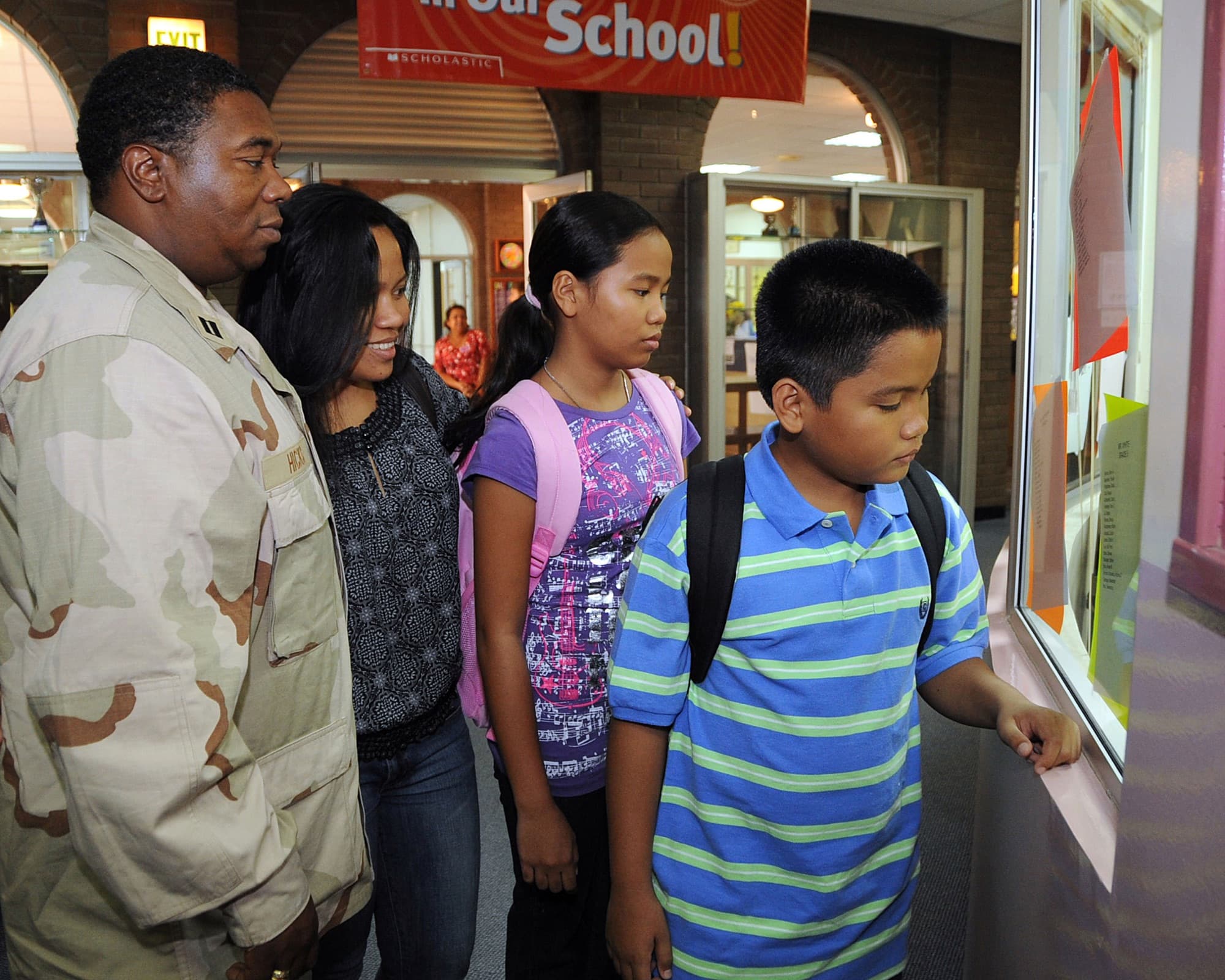 A sailor in uniform checks class schedules with his wife and children on the first day of school