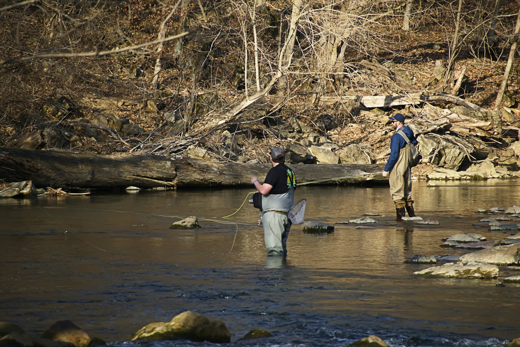 Two men in civilian fishing gear fly fishing a river