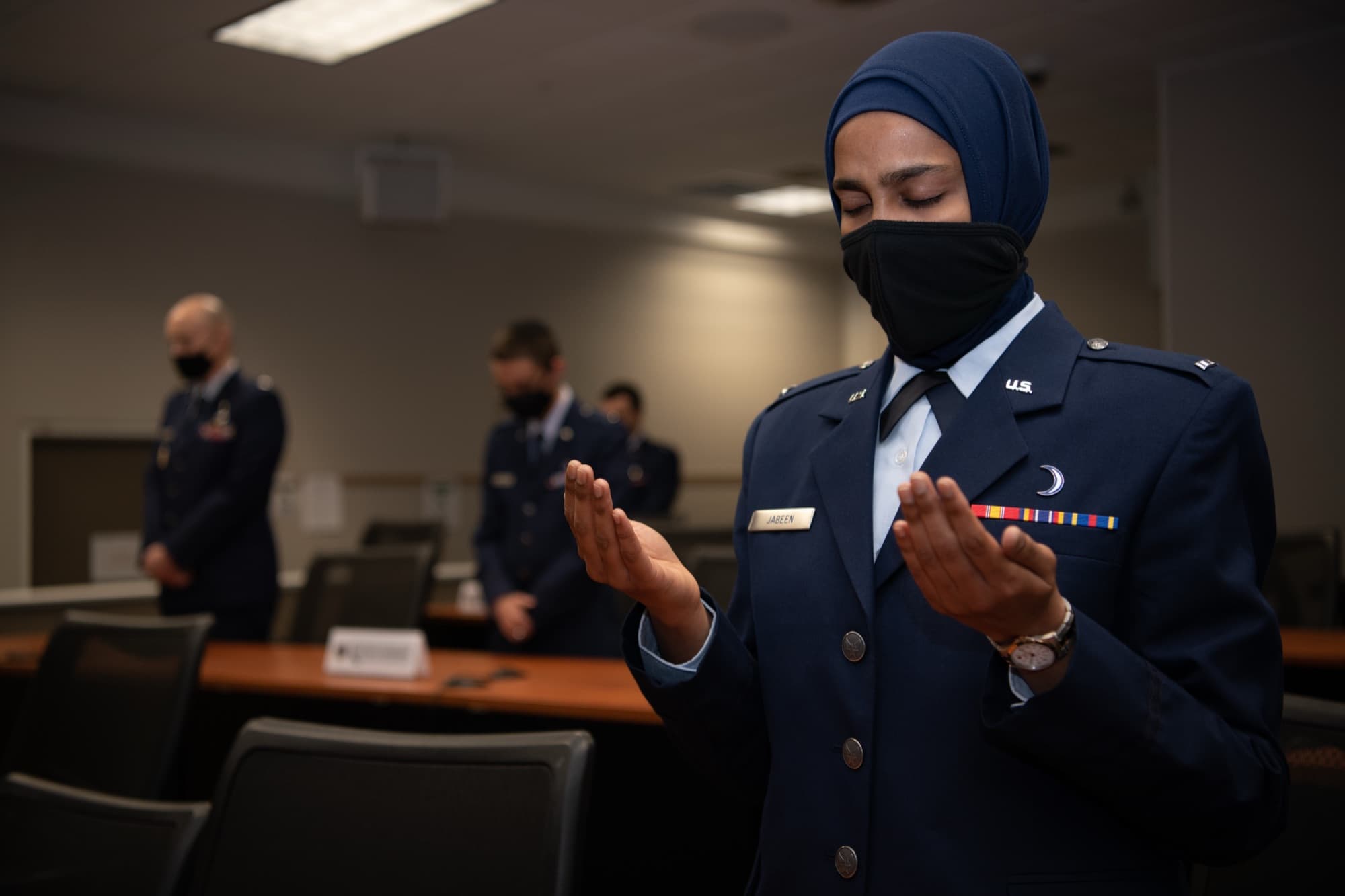 A South Asian woman Air Force chaplain in uniform, wearing a hijab, at prayer