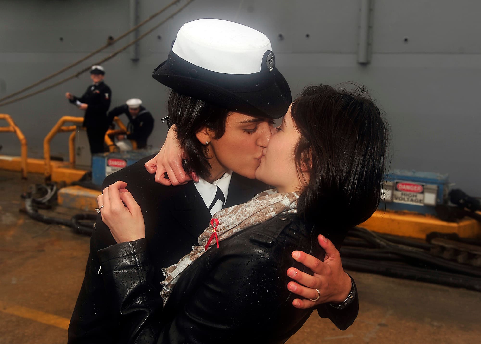 A Navy sailor in dress blues kisses her fiancée on the pier after a homecoming