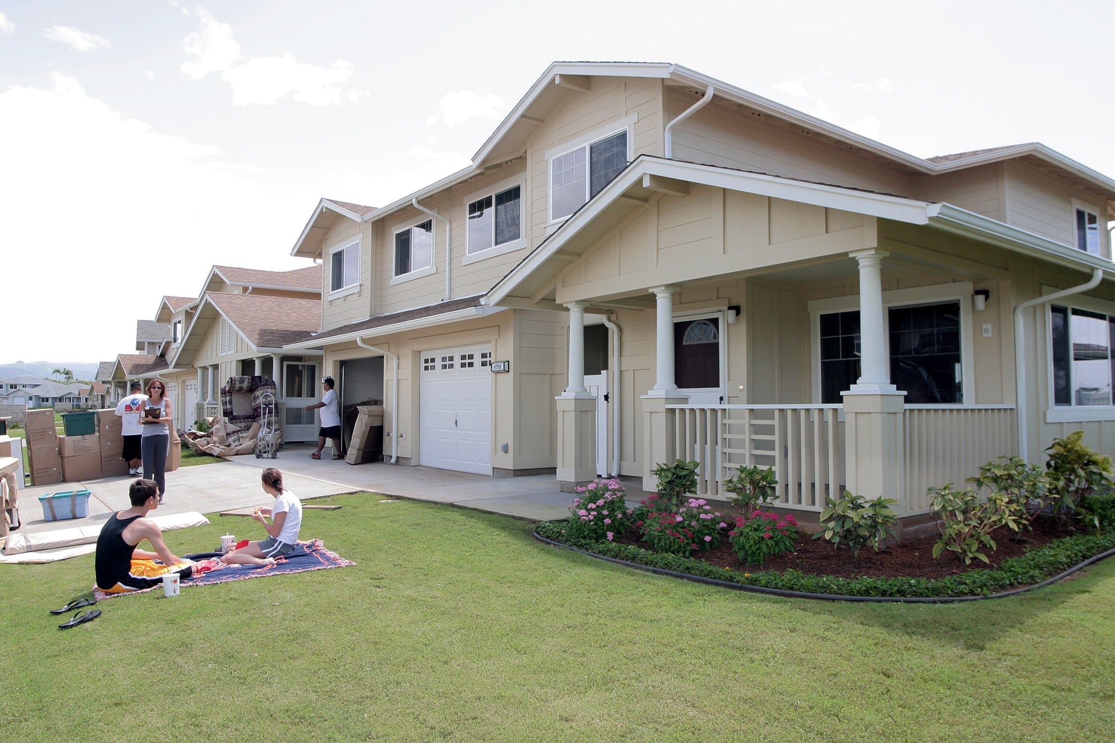 A Navy family sits on the lawn while movers deliver household goods to new housing on Ford Island